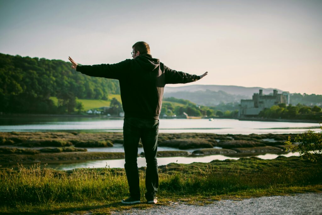 A man stands by the river with arms outstretched, enjoying the scenic view at sunset.