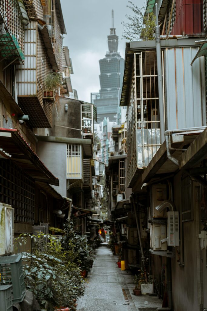 Narrow alleyway in Taipei showcasing residential buildings with a view of a distant skyscraper.