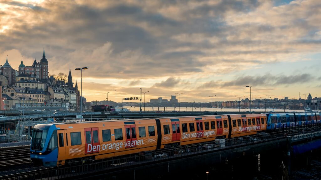 Orange train passing through Stockholm with scenic cityscape at dusk. Urban transport system in Sweden.