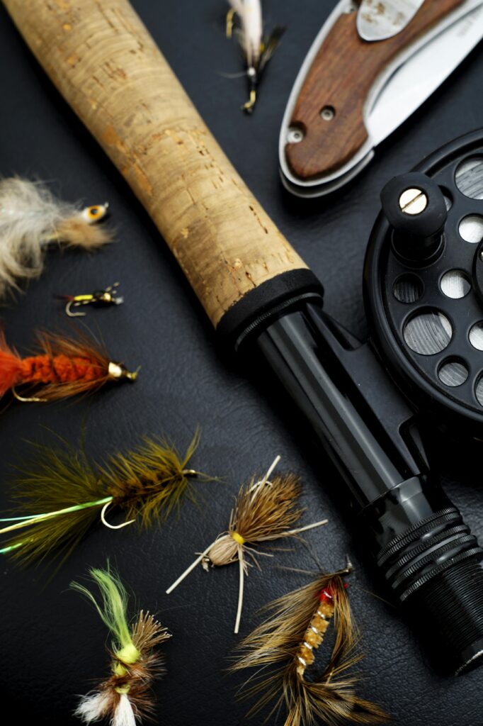 Detailed view of fly fishing gear including rod, reel, and colorful flies on a dark surface.