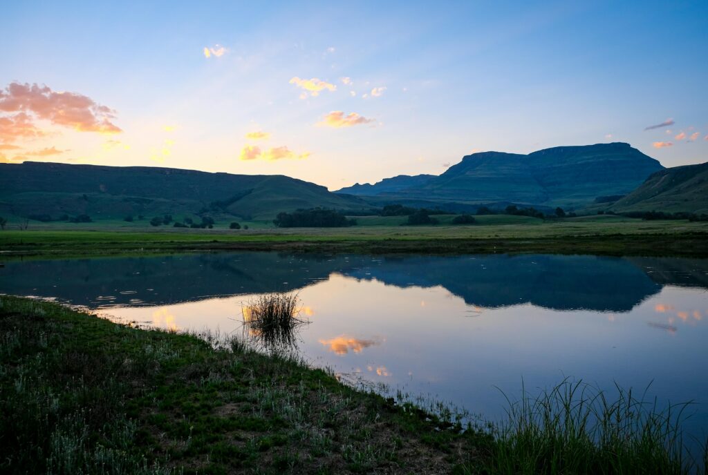 Peaceful sunrise reflecting over a pond with Drakensberg mountains in Himeville, South Africa.