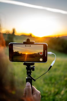 Person recording a beautiful sunset with a smartphone on a selfie stick.