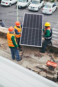 Workers in safety gear installing a solar panel outdoors.