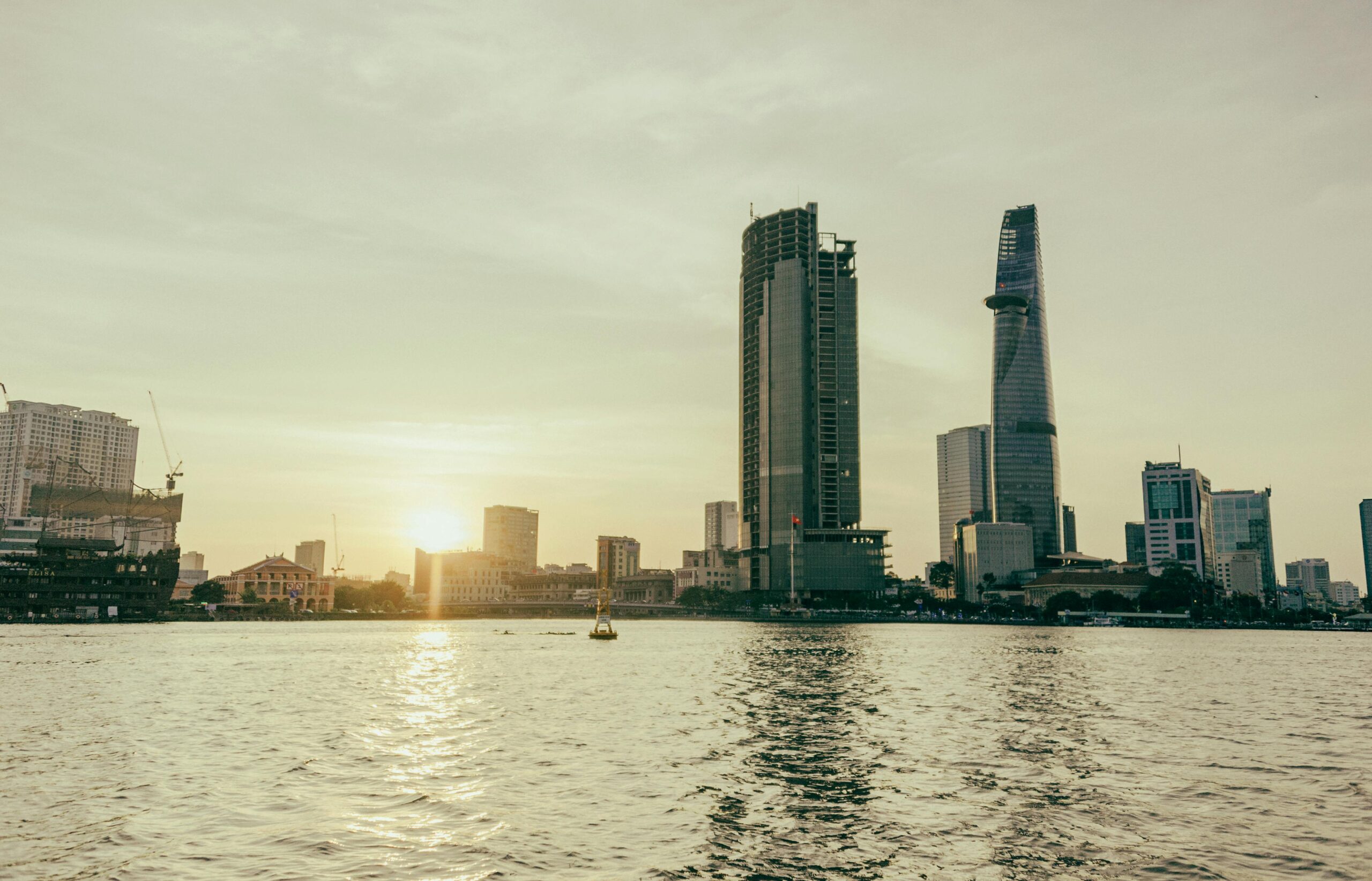 Stunning view of a modern city skyline with skyscrapers by a river during sunset, reflecting serene city life.