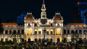 Beautifully illuminated Ho Chi Minh City Hall at night, showcasing iconic architecture and vibrant urban life.